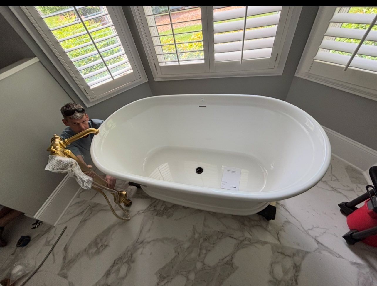 A man is playing a saxophone next to a bathtub in a bathroom.