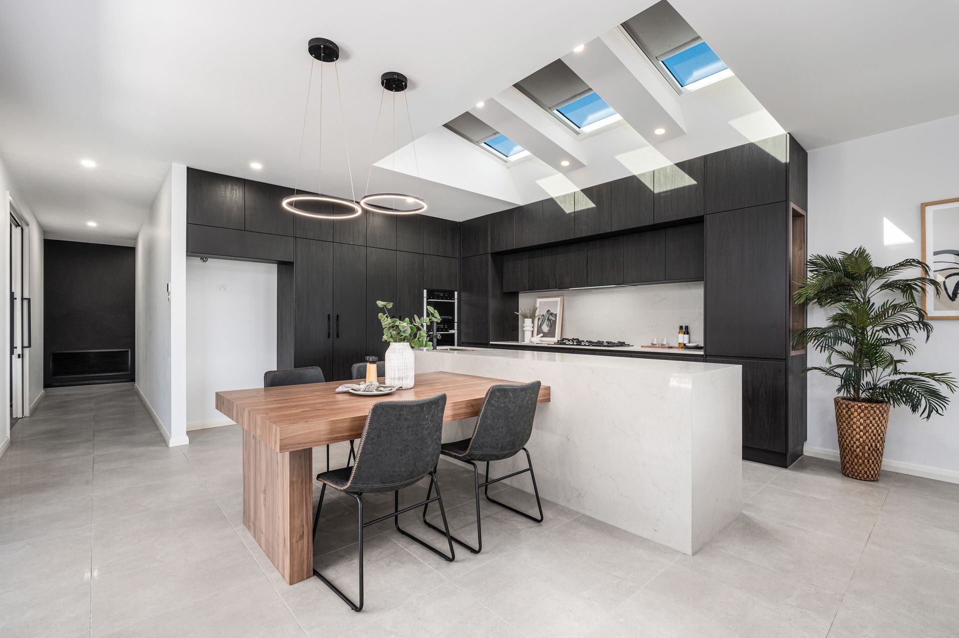 Modern kitchen with black cabinetry, wooden table, and skylights. - Groves Joinery NSW