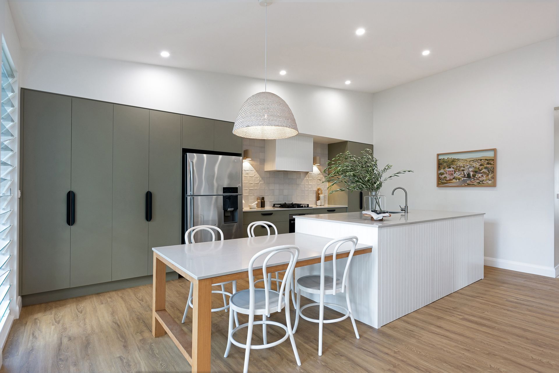 Modern kitchen with dining area; gray cabinets, white island, wooden table with chairs, wicker pendant light.