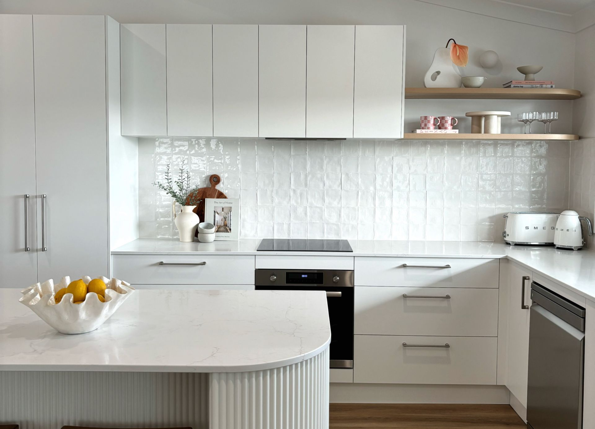 White modern kitchen with island and white cabinetry, a white backsplash, and a built-in oven.