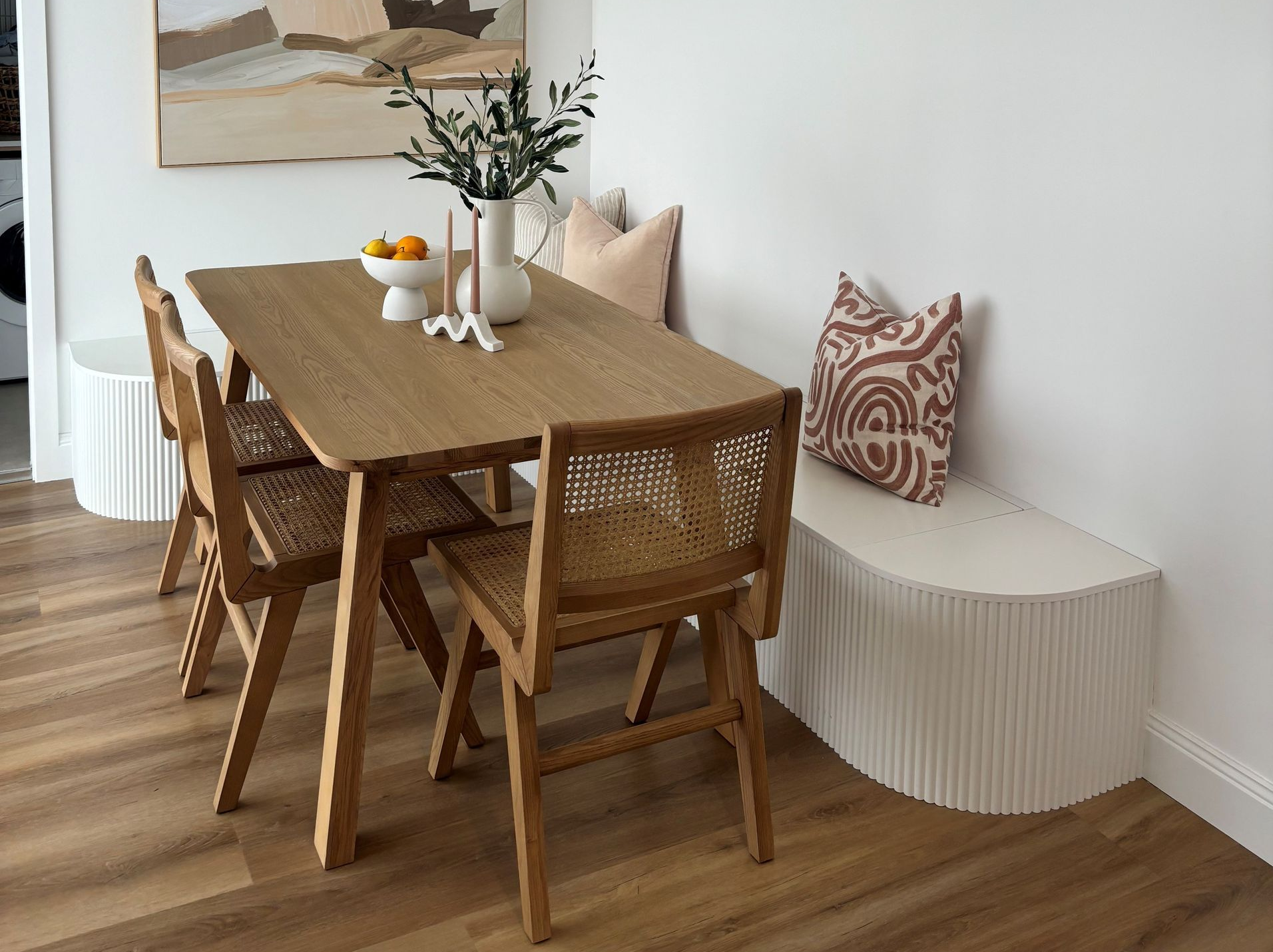 Dining area with wooden table, woven chairs, built-in bench, and artwork.
