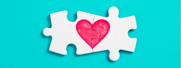 Two puzzle pieces with a heart drawn on them on a blue background.