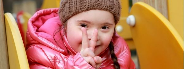 A little girl in a pink jacket and hat is sitting on a slide.