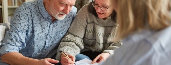 A senior man and a woman meeting with an elder law attorney are signing a legal document.