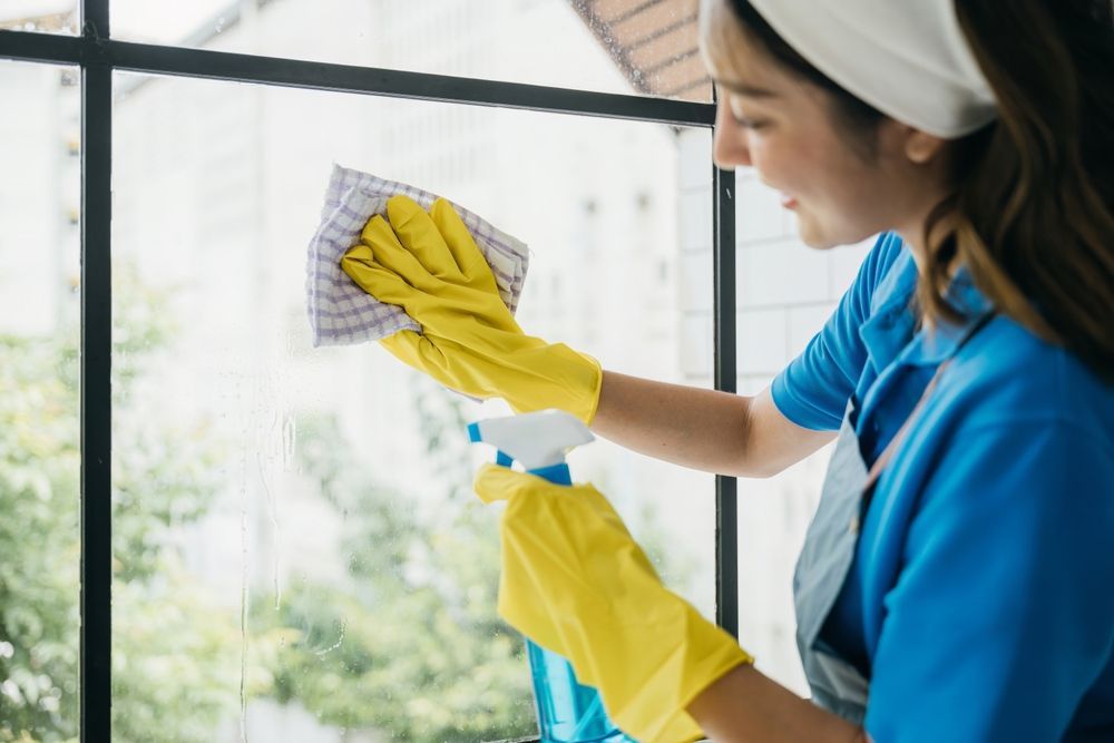 Woman in yellow gloves cleaning window with spray bottle and cloth.