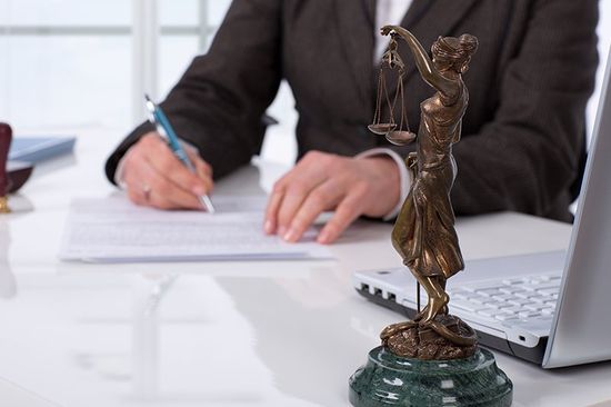 un uomo alla scrivania mentre scrive e una statuetta che impugna una bilancia a due piatti