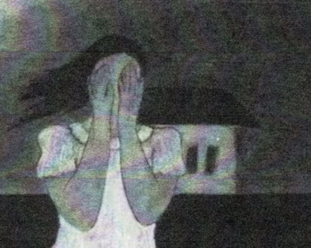 A woman is covering her face with her hands in front of a house.
