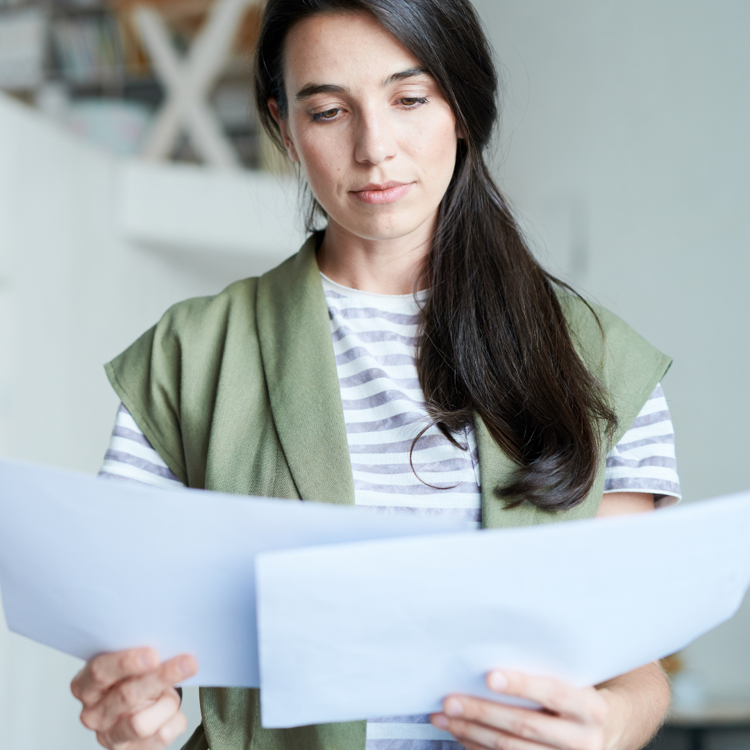 A woman in a green vest is reading a piece of paper