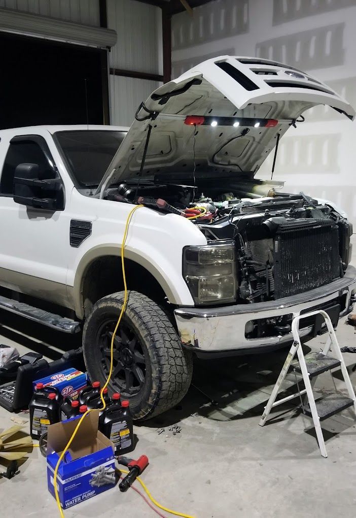 Mechanic in blue overalls working on car engine, hood open.