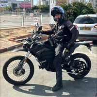 גבר עומד ליד אופנוע במגרש חניה.