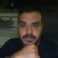 גבר עם זקן יושב ליד שולחן עם ידו על סנטרו.