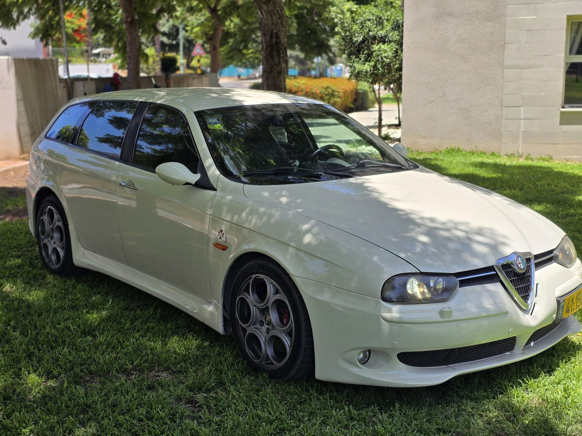 מכונית לבנה חונה בדשא מול בניין.