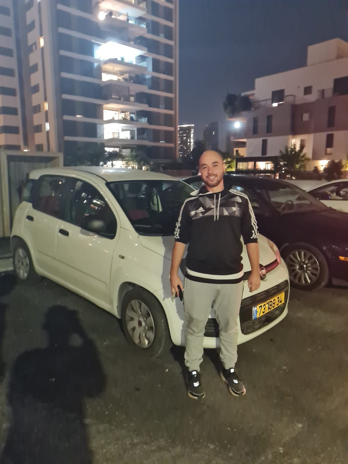 גבר עומד מול מכונית לבנה שעליה לוחית רישוי שכתוב עליה 'tf'