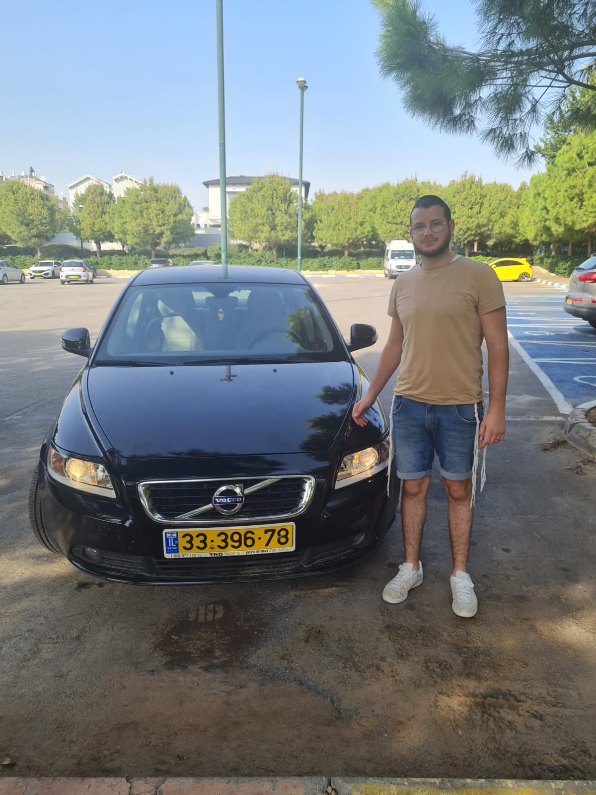 גבר עם קביים עומד מול מכונית וולוו שחורה.