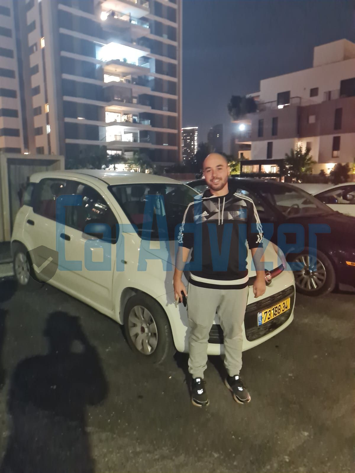 גבר עומד מול מכונית לבנה ועליה לוחית רישוי שכתוב עליה 'tsf'