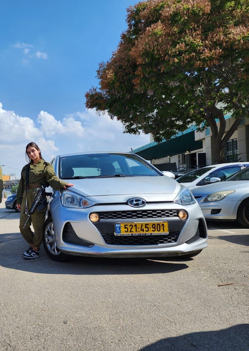 אישה במדי צבא עומדת ליד מכונית כסופה.