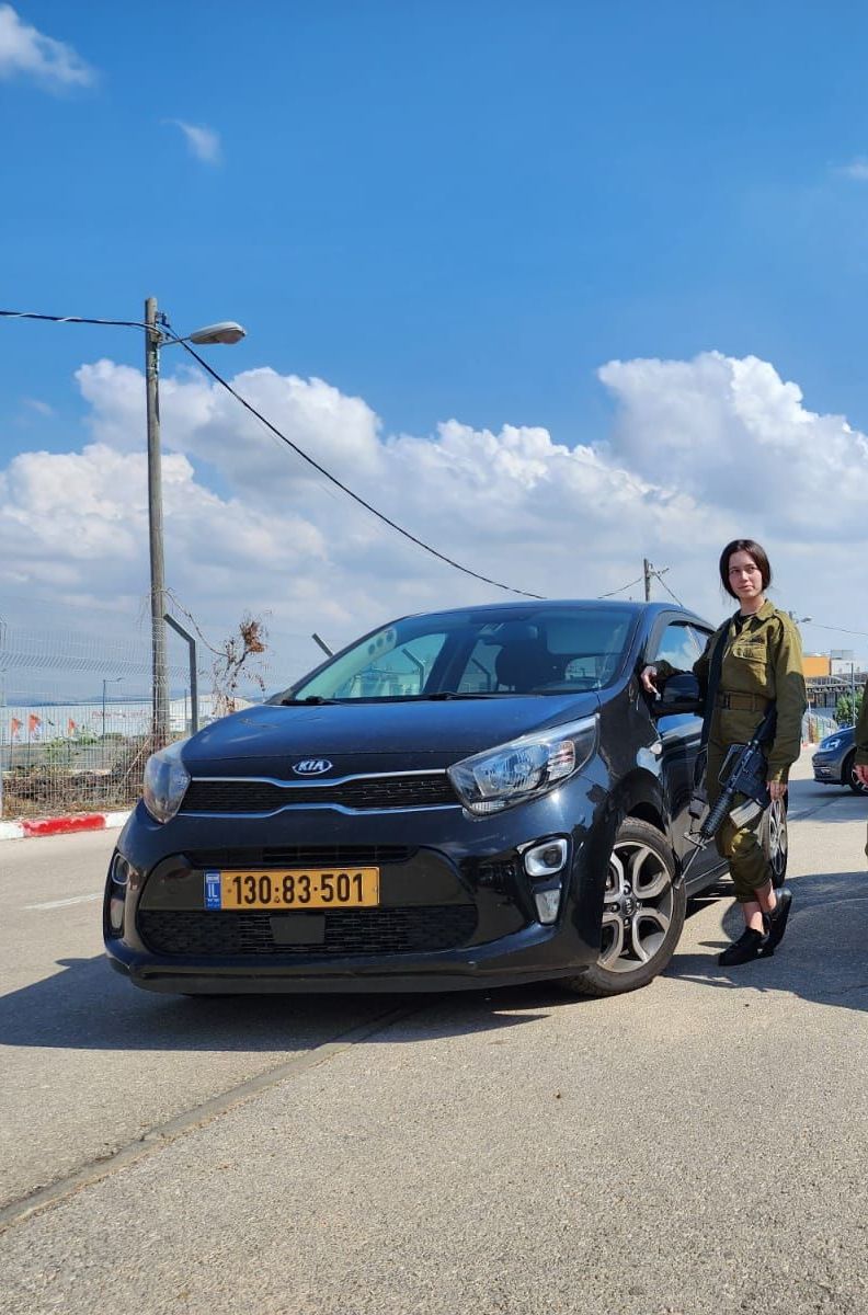 אישה במדי צבא עומדת ליד מכונית שחורה.
