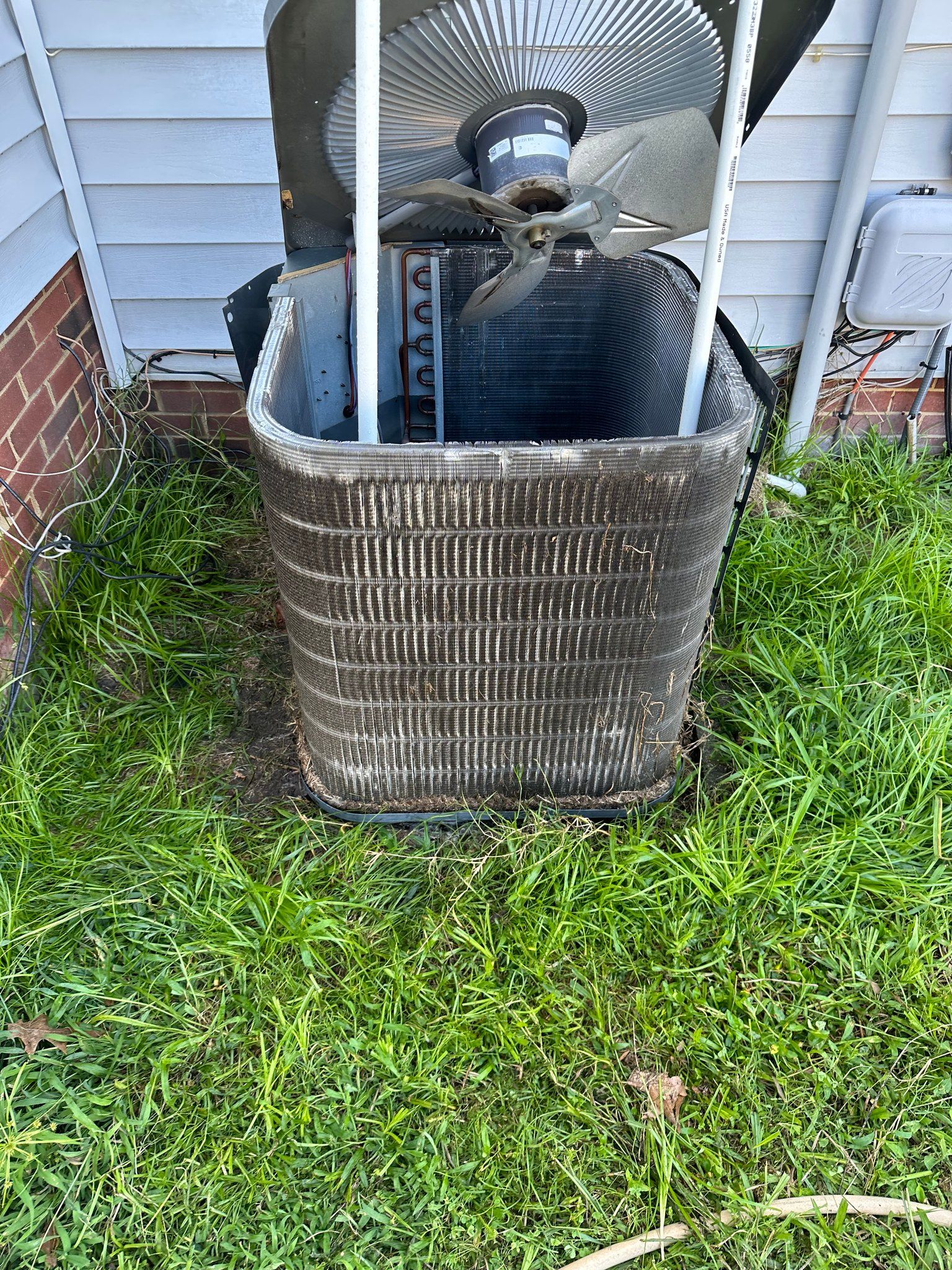 A dirty air conditioner is sitting in the grass next to a house.