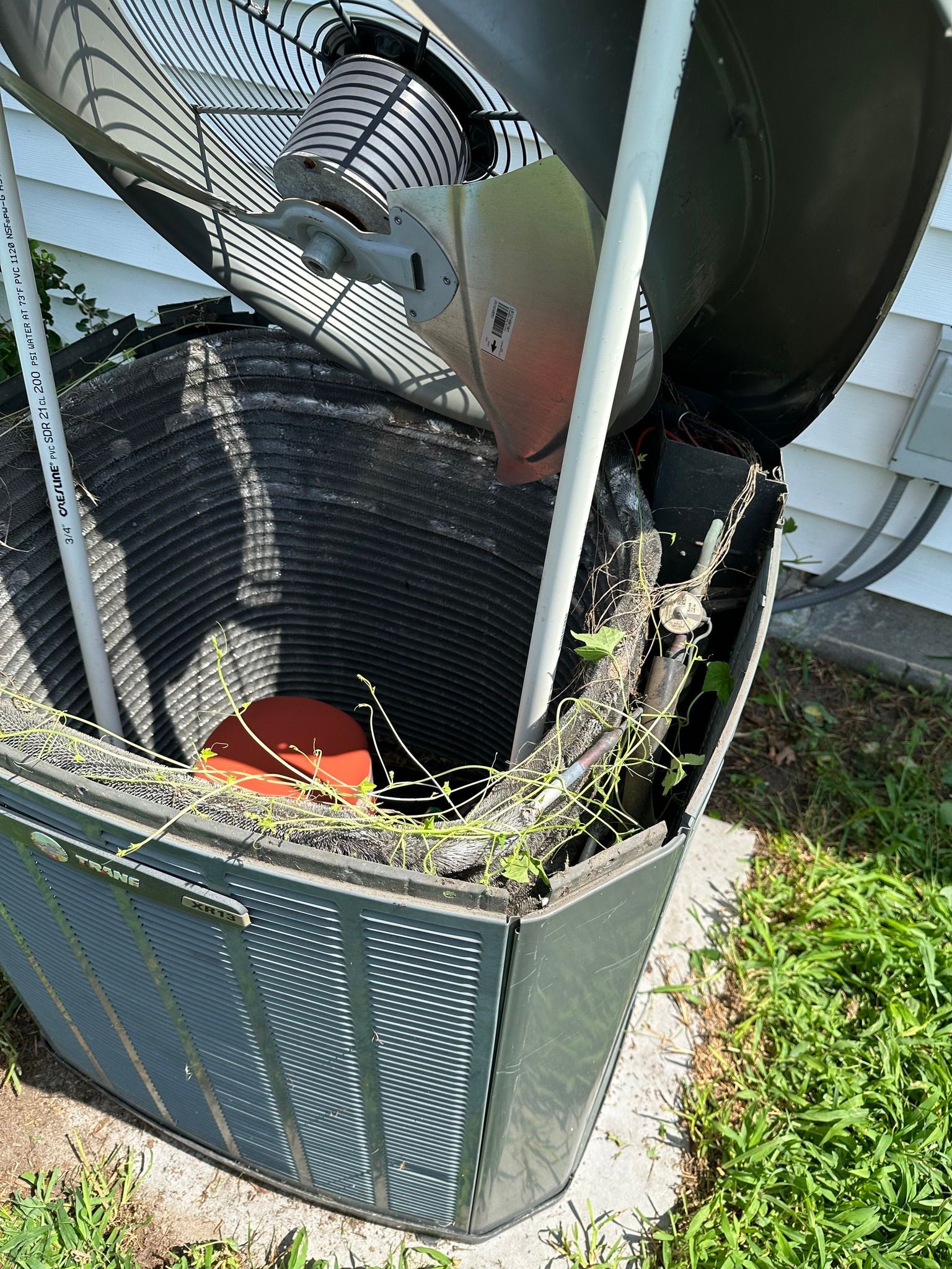 A broken air conditioner is sitting in the grass next to a house.