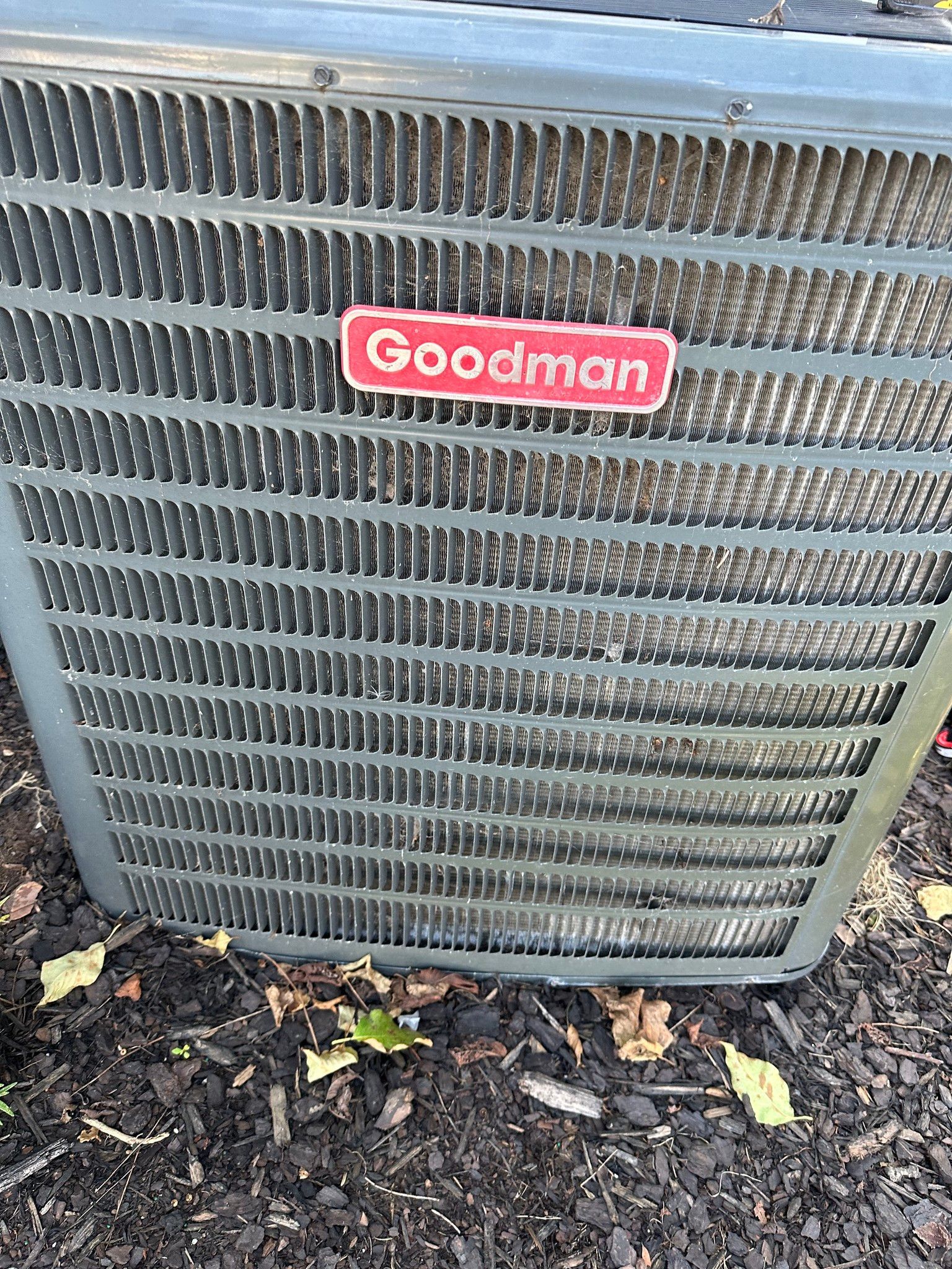 A goodman air conditioner is sitting on the ground.