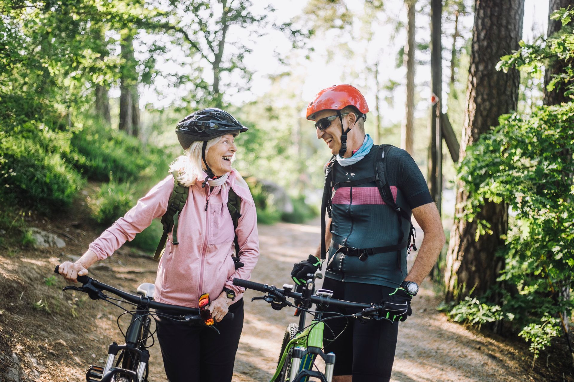 Two cyclists, smiling, in a forest, next to their bikes.