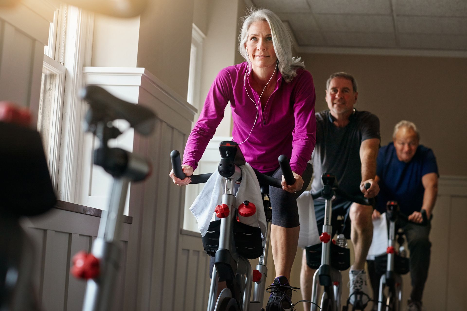 Group of people, exercising on stationary bikes in a brightly lit gym.