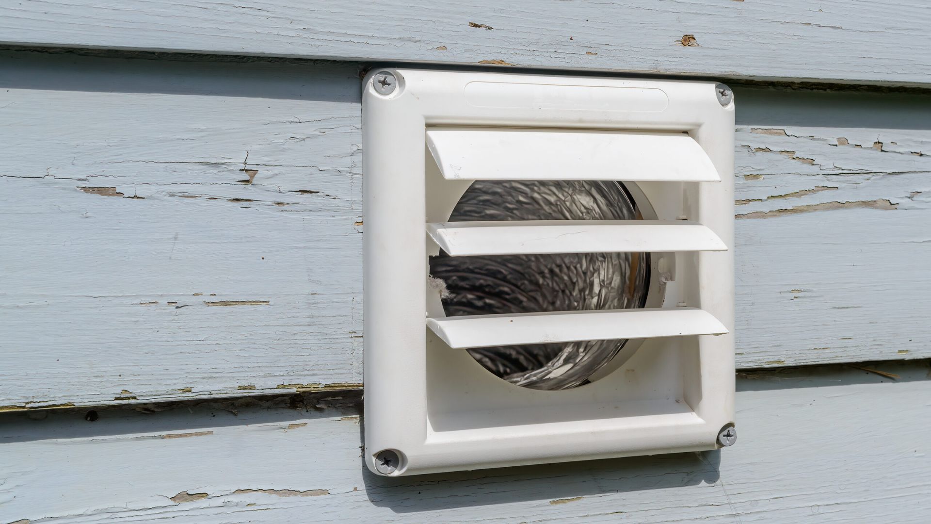 A white vent is installed on the side of a house.
