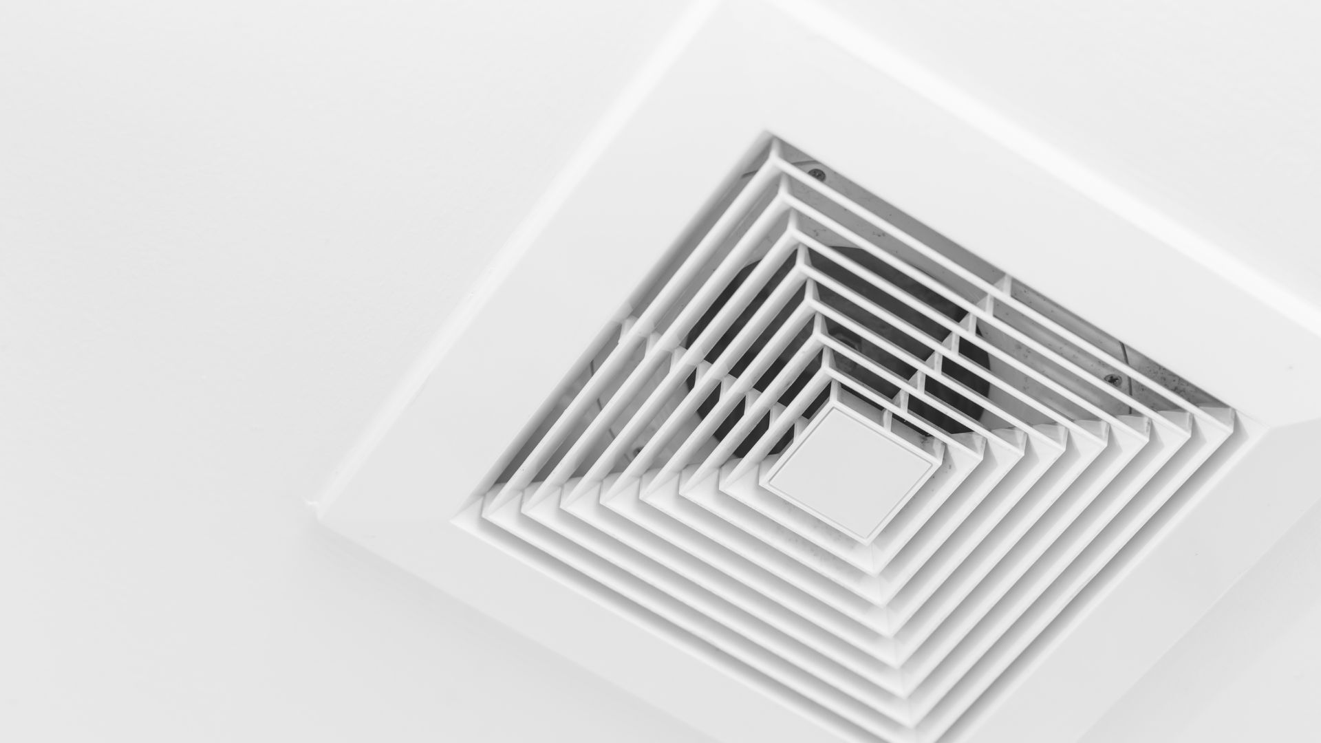 A close up of a white ceiling fan on a white wall.