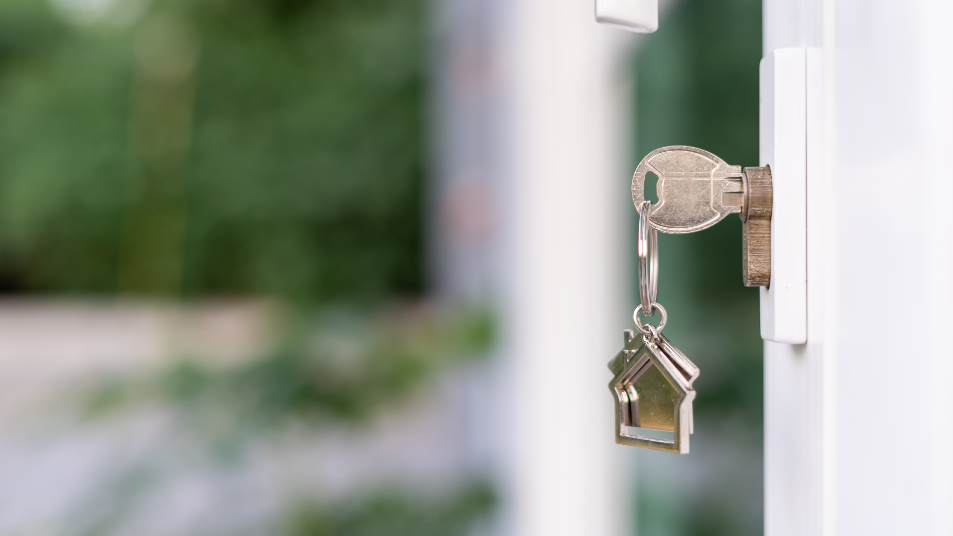 A key is hanging from a keyhole with a house keychain attached to it.
