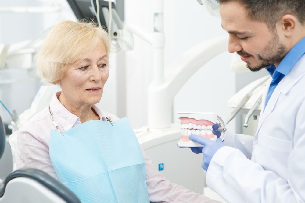 Dentist showing a senior woman a dental model during a consultation, explaining treatment options