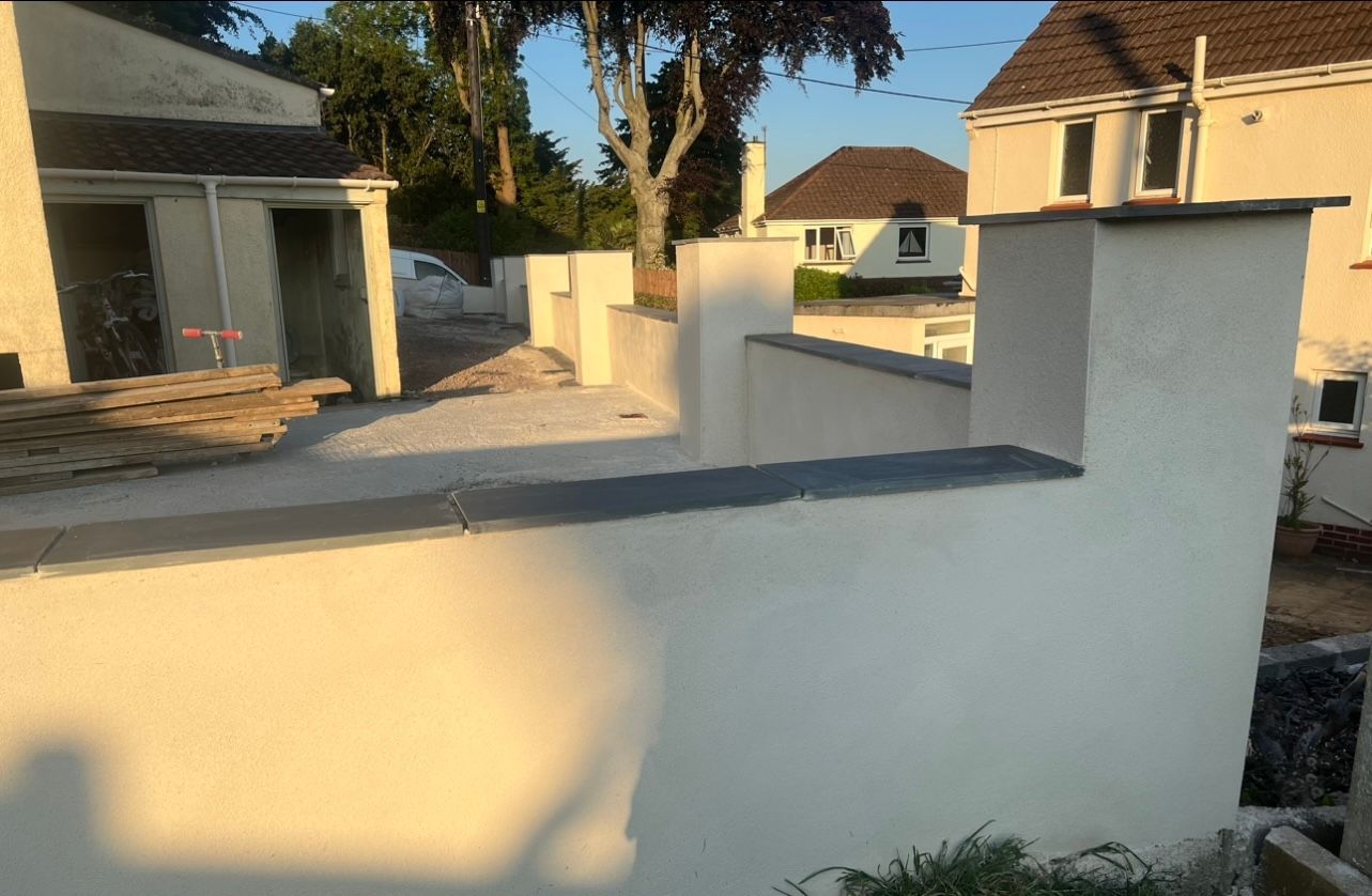 A white wall with a chimney on top of it in front of a house.