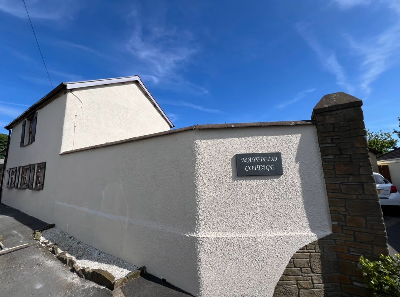 A white house with black trim and windows is sitting on top of a lush green field.