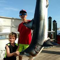 Two young boys are standing next to a large shark on a dock.