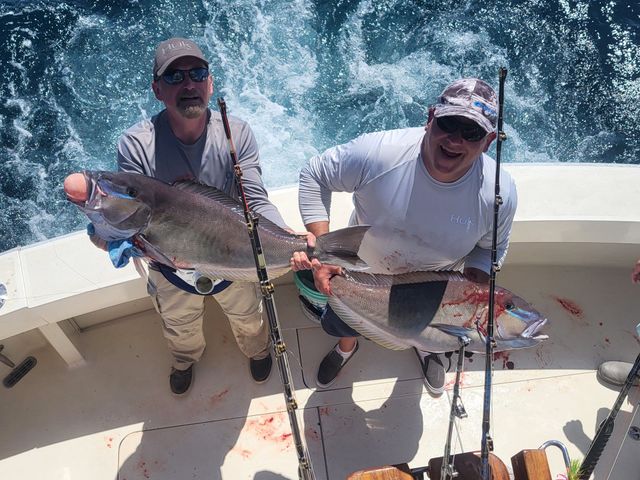 Two men on a boat holding a large fish