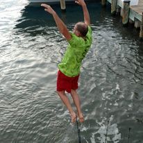 A man is jumping into the water from a dock.