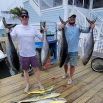 Two men are standing on a dock holding fish.