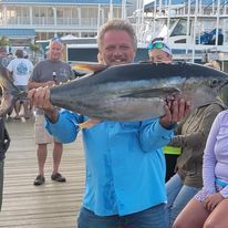 A man in a blue shirt is holding a large fish on a pier.