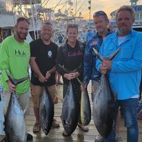 A group of people are standing on a dock holding fish.