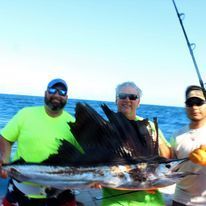 Three men are standing on a boat holding a large fish.