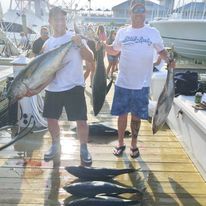 Two men are standing on a dock holding large fish.