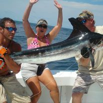 A group of people are standing on a boat holding a large fish.
