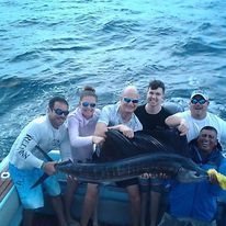 A group of people are sitting on a boat holding a large fish.