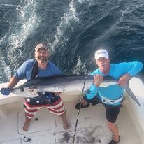 Two men are standing on a boat holding a large fish.