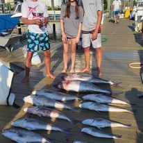 A group of people standing next to a pile of fish on a dock.