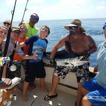 A group of people are standing on a boat in the ocean holding fishing rods.