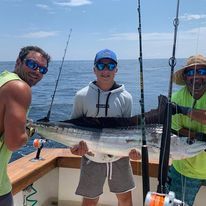Three men are standing on a boat holding a large fish.