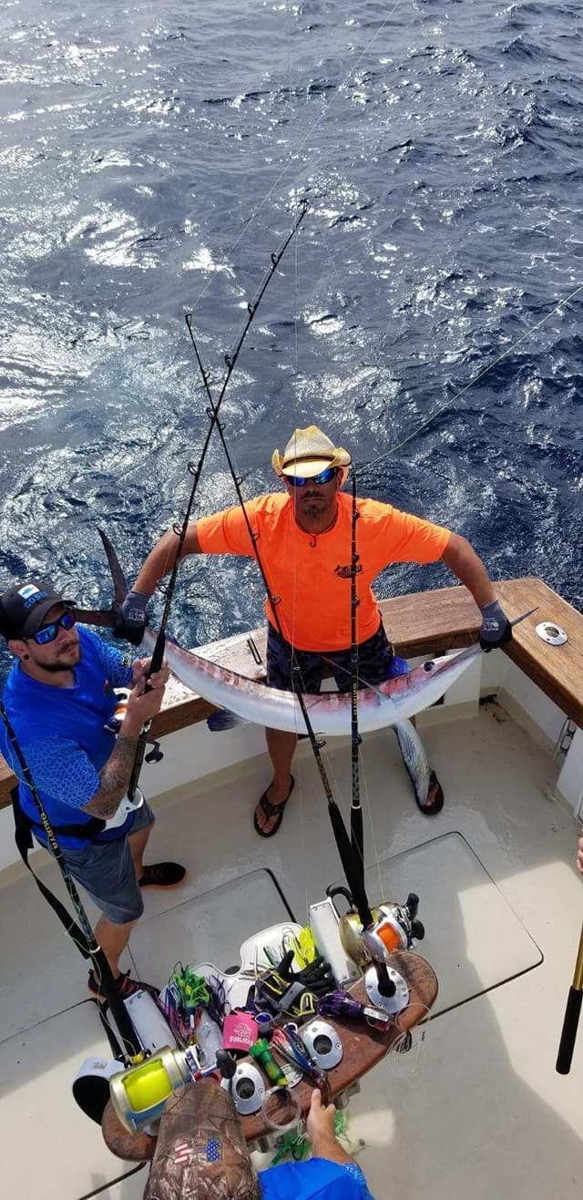 Two men are standing on a boat holding fishing rods and a large fish.