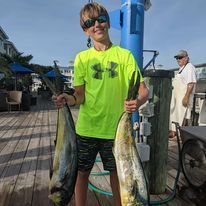 A young boy is holding two large fish on a dock.