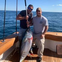 Two men are standing on a boat holding a large fish.