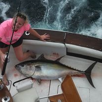A woman is kneeling on a boat holding a large fish.